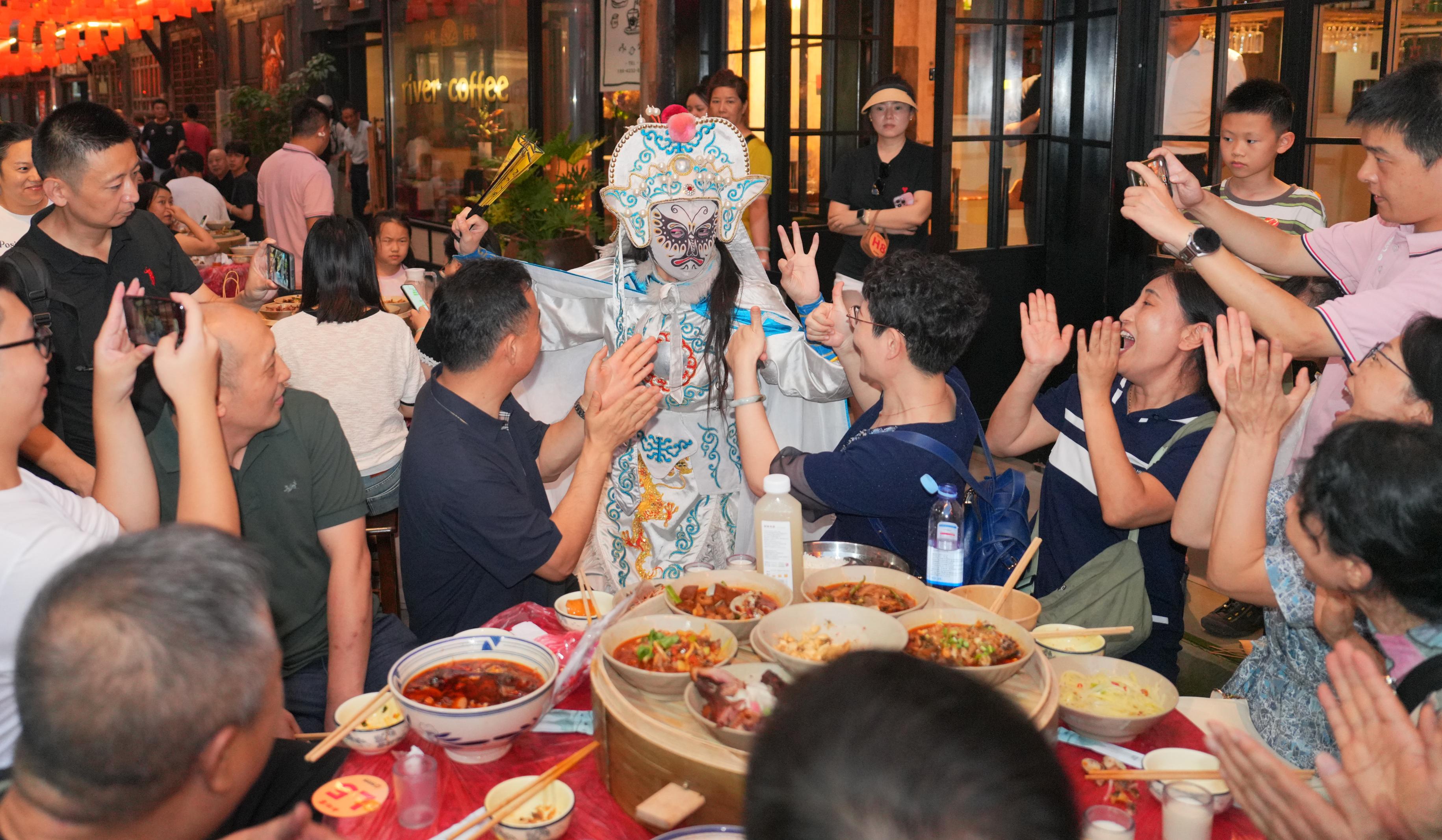 ▲在偏岩古镇的长街宴上,川剧变脸演员和游客互动。新华社发(秦廷富摄)